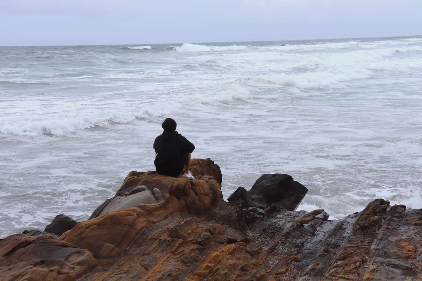 Student meditates while gazing onto a tumultuous ocean landscape