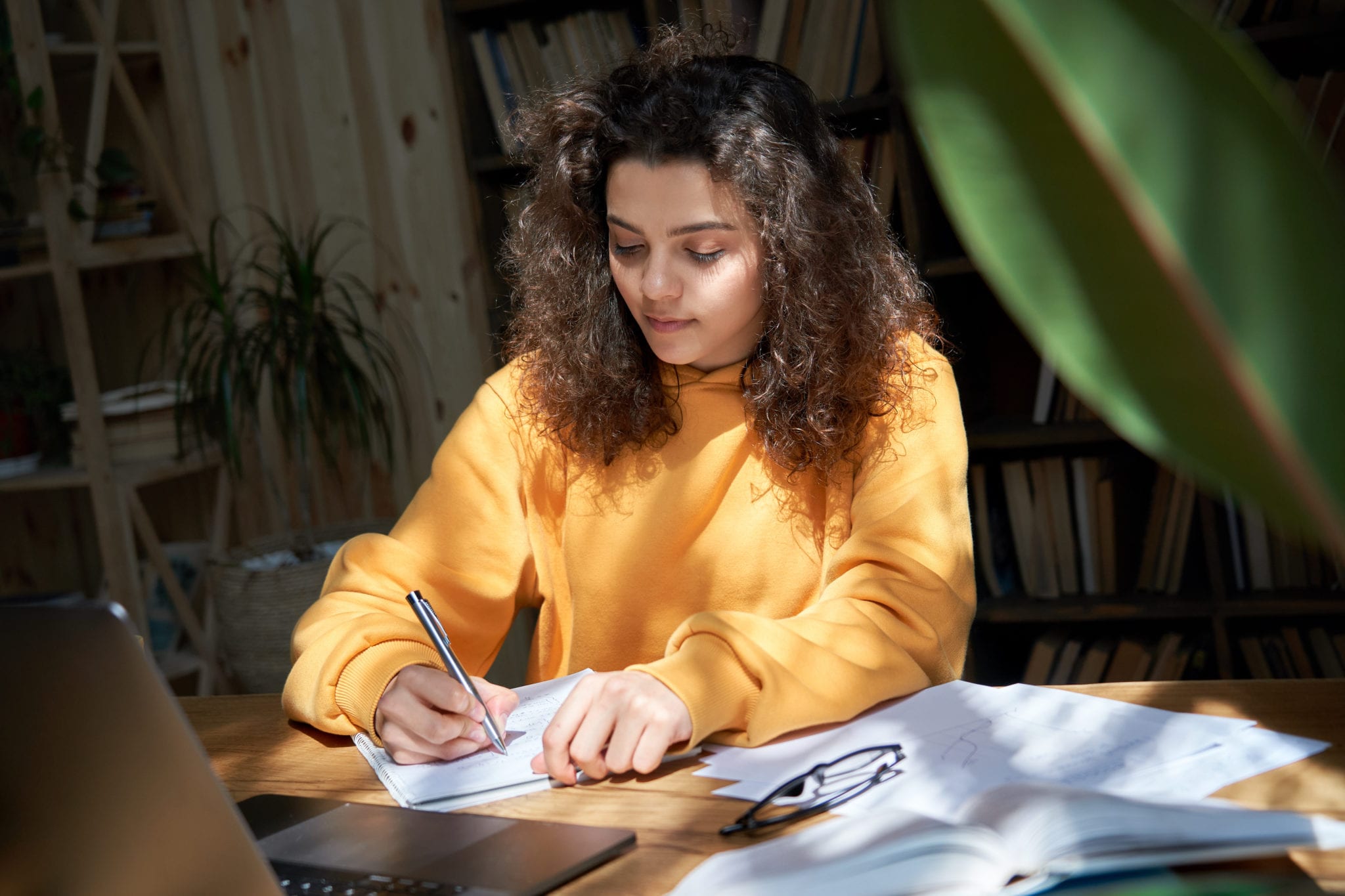 teen girl high school study from home distance learning taking notes doing homework in sunny room. Latinx teen distance learning online on laptop elearning remote..